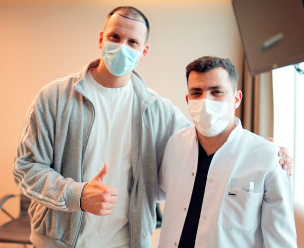 Patient giving a thumbs up standing next to doctor, preparing for hair transplant procedure