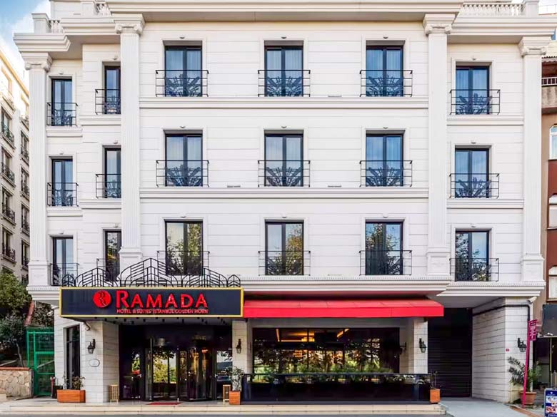 The white exterior of the hotel with red lettering that says Ramada.
