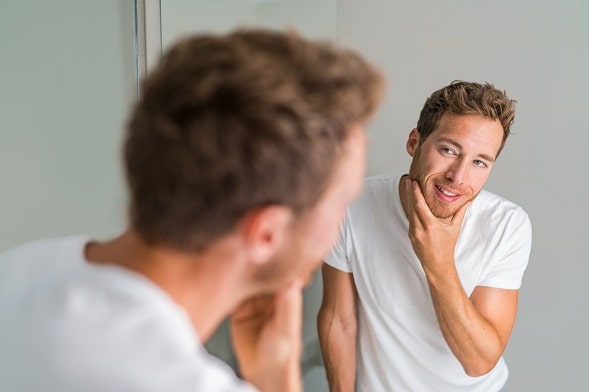 Hombre observando su barba en el espejo Trasplante de Barba