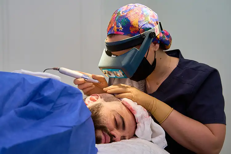 Ein Mann liegt auf einem Behandlungstisch und wird von einer Frau während einer Haartransplantation behandelt.