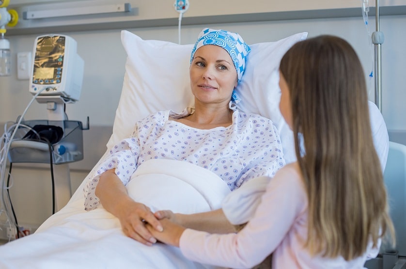 Frau mit Krebs liegt im Krankenbett und bekommt Besuch von Ihrer Tochter