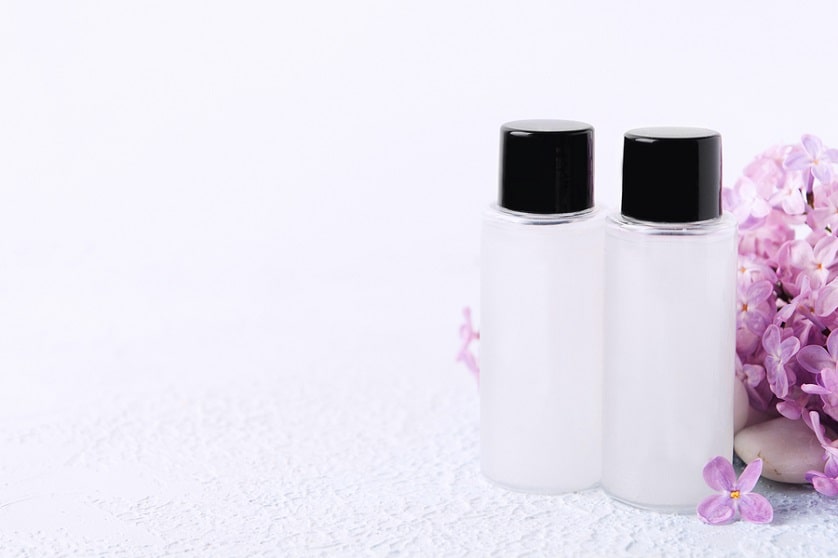 2 Shampooflaschen auf weißem Hintergrund neben einer pinken Pflanze