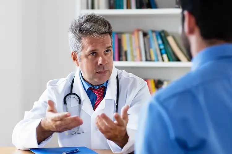 Ein Arzt spricht mit einem Patienten. Vor ihm liegen eine Mappe und ein Stift.