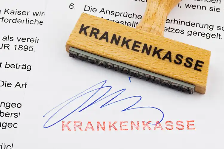 Ein Stempel mit der Aufschrift “Krankenkasse” liegt auf einem unterschriebenen Antrag.