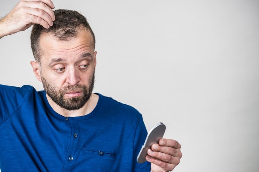 Mann schaut Fettige Haare im Spiegel