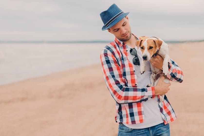 Mann mit Hut am Strand mit Hund