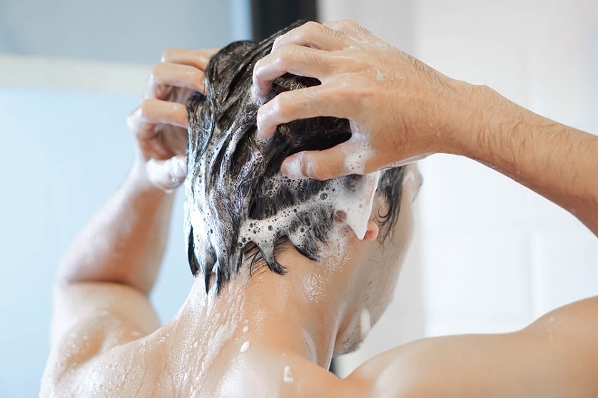 Mann shampooniert sich die Haare unter der Dusche