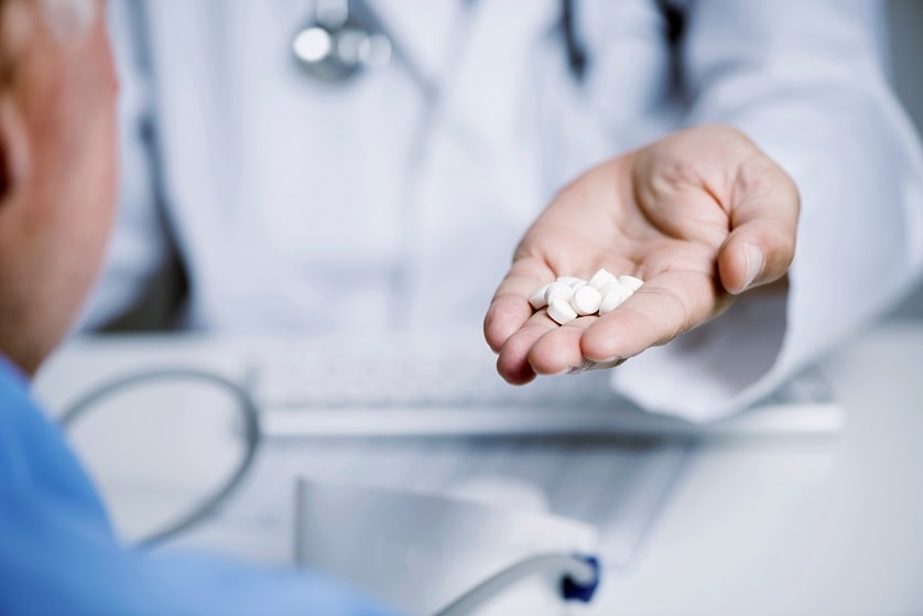 Arzt reicht einem Patienten eine handvoll Tabletten