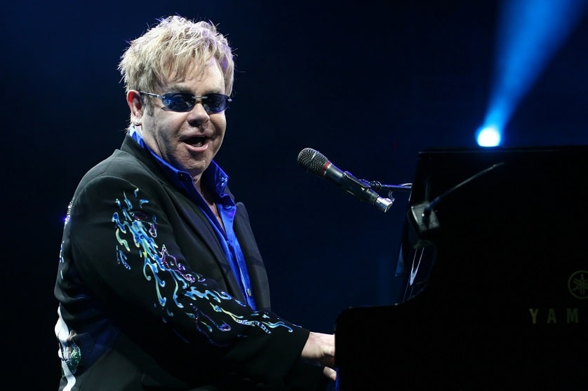 Elton John sitzt am Klavier bei einem Konzert und zeigt das Ergebnis der Haartransplantation bei einem Promi