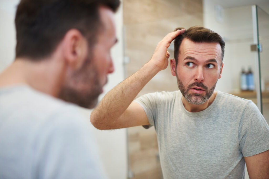 Ein Mann schaut in den Spiegel und betrachtet seine Haare