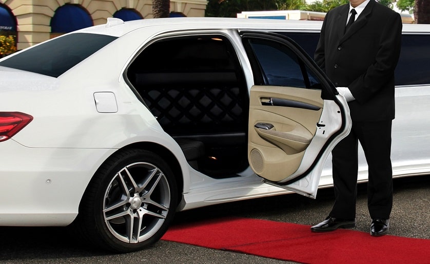 Eine weiße Limousine mit Chauffeur, der die Tür öffnet, vor dem roten Teppich