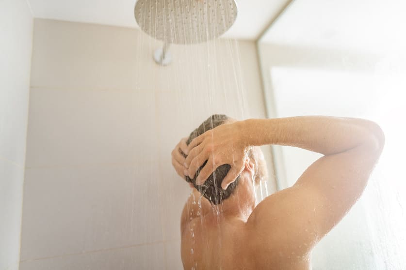 Mann steht unter der Dusche und wäscht sich die Haare