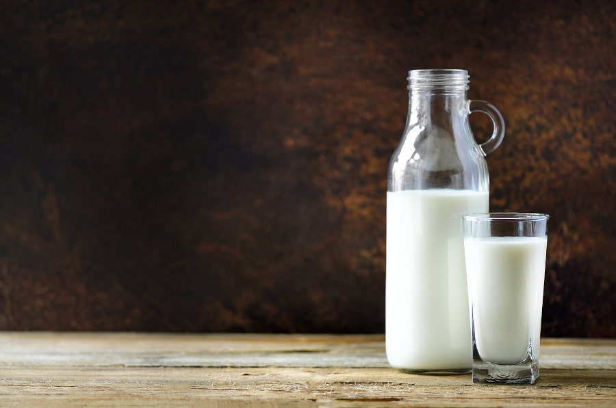 Eine Glasflasche Milch steht neben einem Glas gefüllt mit Milch