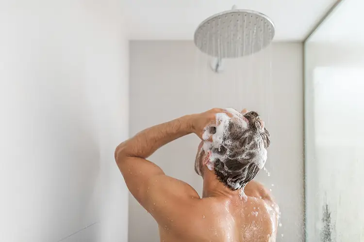 Ein Mann steht unter der Dusche und shampooniert seine Haare ein