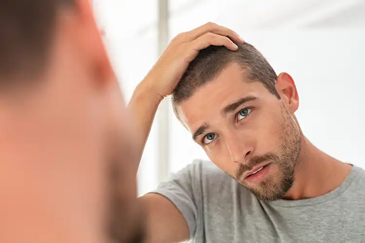 Lamotrigin: Ein Mann mit kurzen Haaren schaut in den Spiegel und begutachtet sein Haar.
