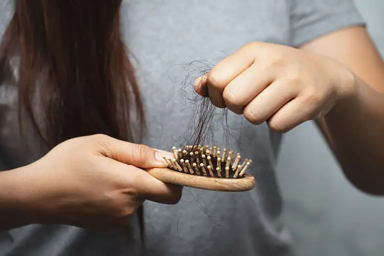 Eine Frau zieht einen Büschel Haare aus einer Bürste 