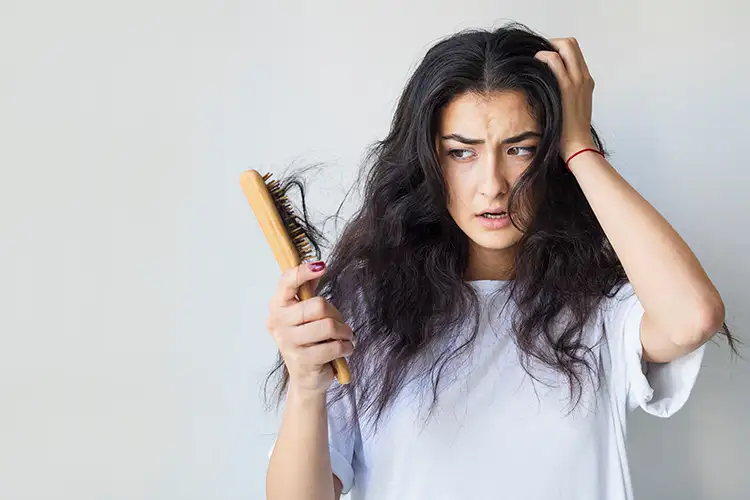 Eine Frau fasst sich mit einer Hand an den Kopf und hält in der anderen Hand eine Bürste voller Haare.