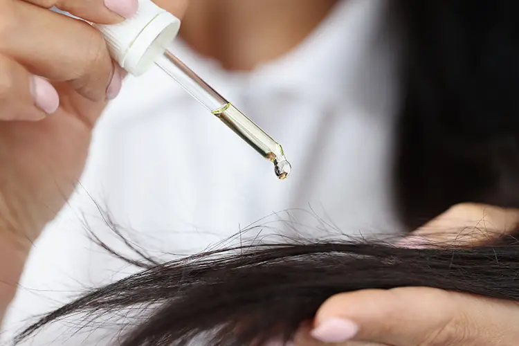 Eine Frau träufelt sich mit einer Pipette einige Tropfen Rizinusöl auf ihre Haarspitzen.