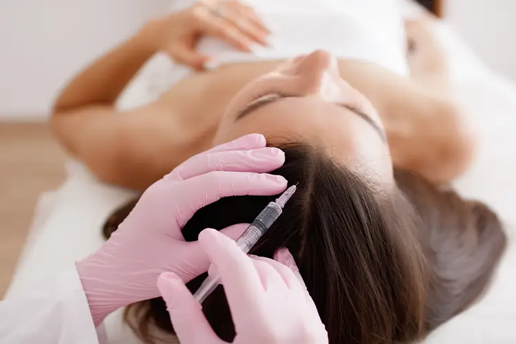 Eine Frau liegt auf einer Behandlungsliege und erhält eine Mesotherapie Behandlung. An ihrem Kopf hält eine zweite Person eine feine Spitze.
