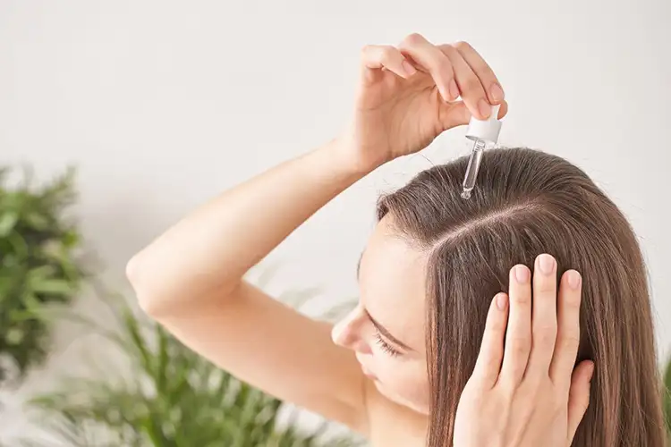 Mit einer Pipette tropft sich eine Frau ein Produkt auf ihren Haaransatz